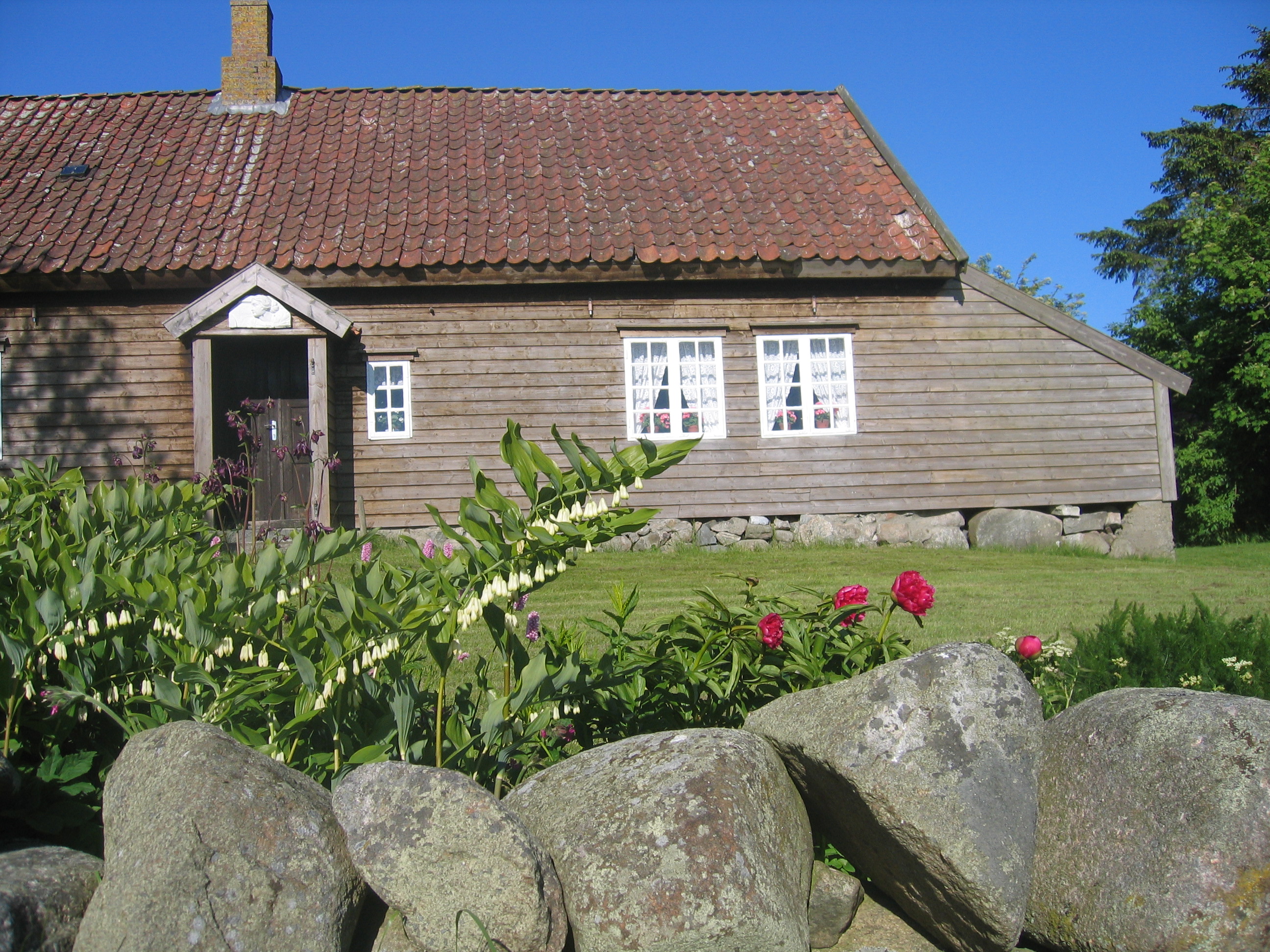 Eit av dei gamle husa på Grødalandstunet, med steingard og blomar framfor